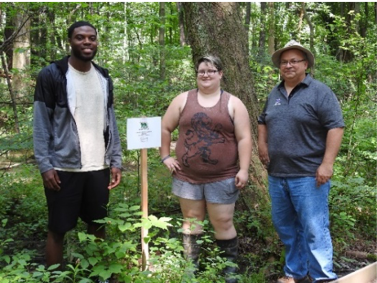 Two students and a faculty member stand next to sign near a Nature Center trail